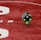 Two green dice with rounded edges are positioned on a red surface that seems to be part of a game board. The surface has white text and numbers on it, including the word 'LUCKYTOPSPIN' in capital letters.