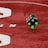 Two green dice with rounded edges are positioned on a red surface that seems to be part of a game board. The surface has white text and numbers on it, including the word 'LUCKYTOPSPIN' in capital letters.