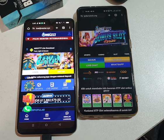 Two smartphones are displayed on a white surface, both showing gambling websites with colorful graphics, text, and various options for logging in and accessing games. The screens are bright and filled with promotional content related to casino and slot games.